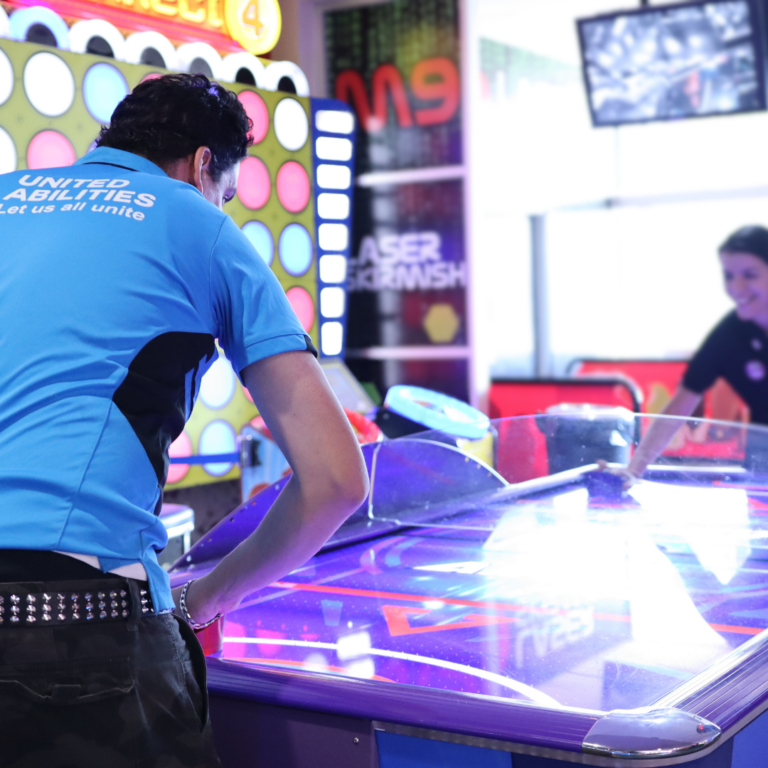 NDIS participant playing air hockey with a United Abilities support worker.